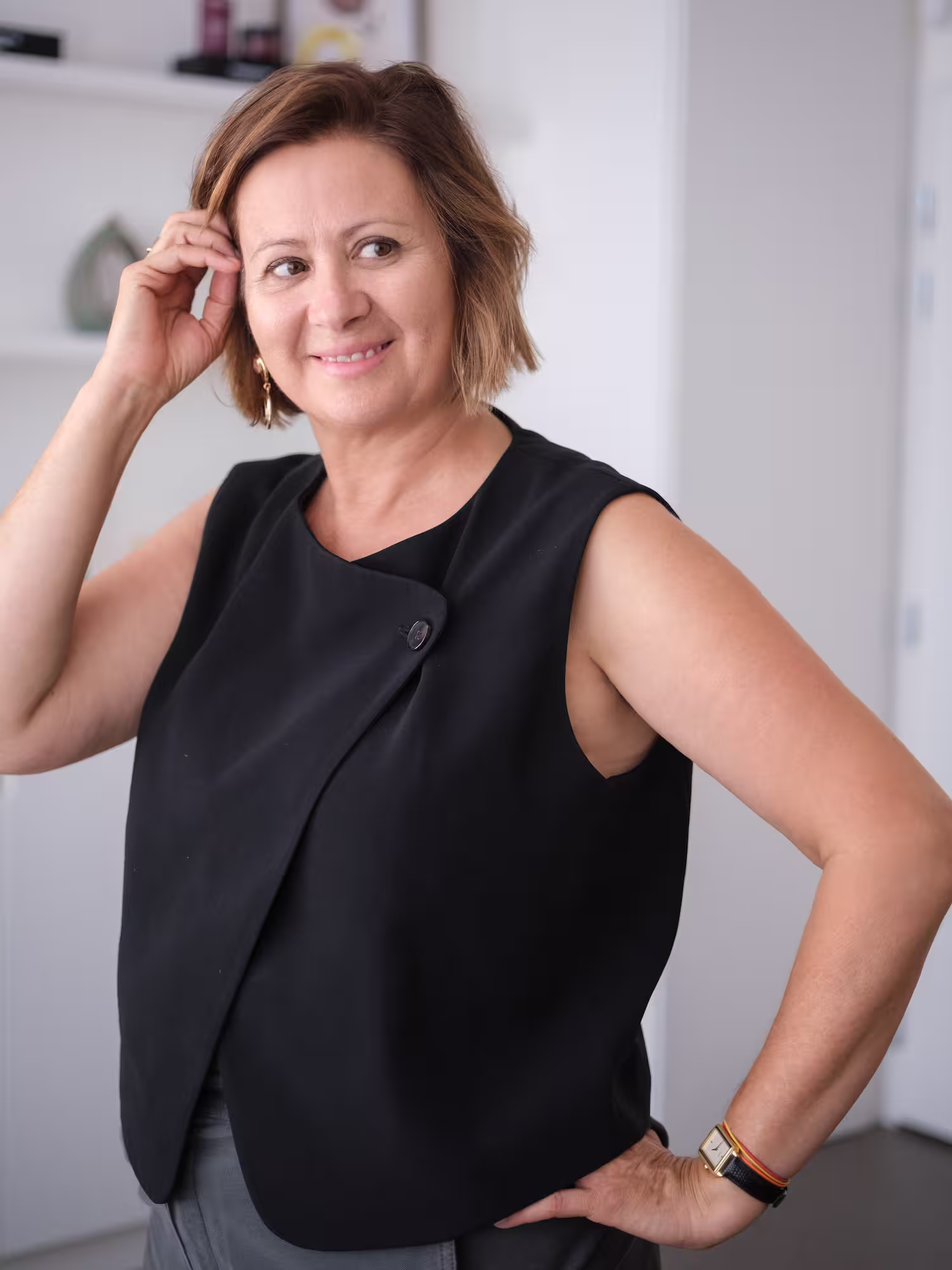 Smiling woman with short brown hair in black blazer standing with arms crossed in office.