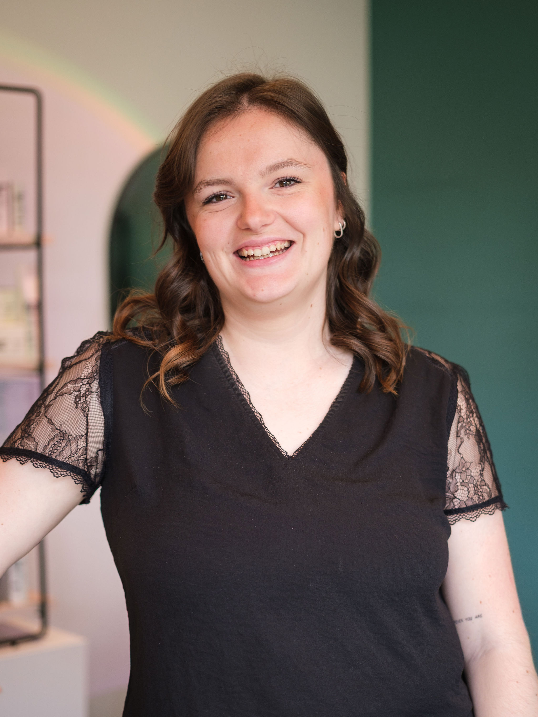 Smiling woman with brown curly hair wearing a black shirt with lace sleeves indoors.