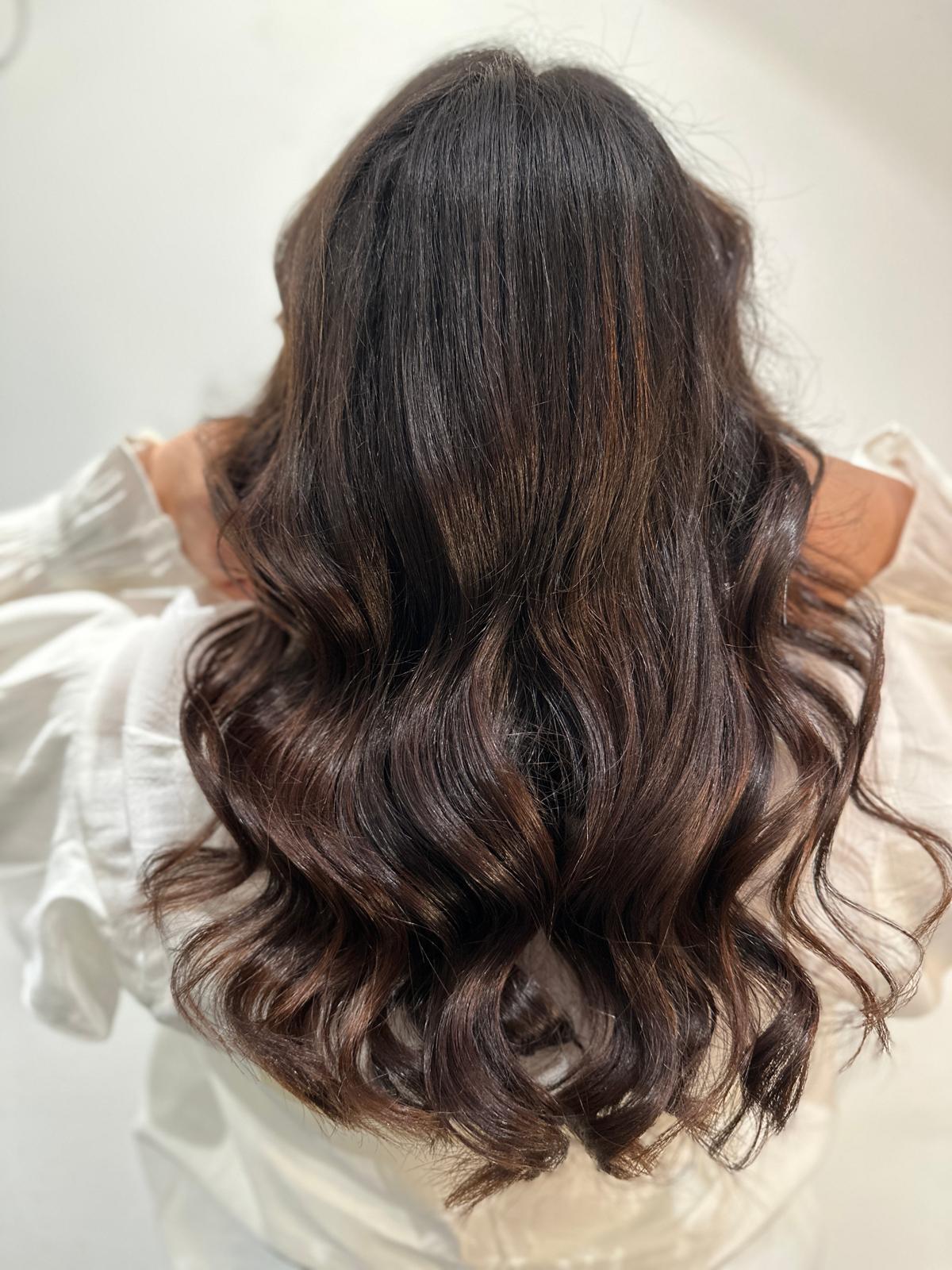 Long dark brown wavy hair with subtle highlights on a person wearing a white shirt.