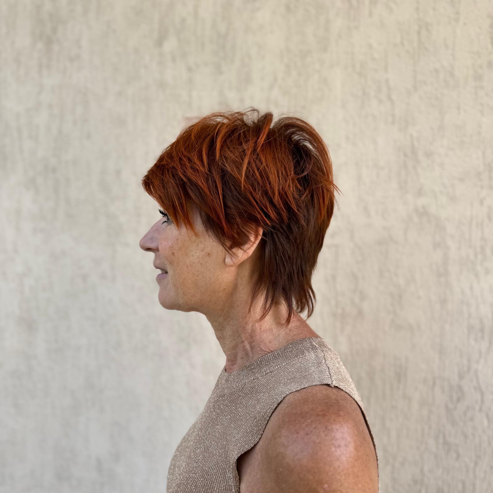 Side profile of a middle-aged woman with short red hair wearing a sleeveless beige top.