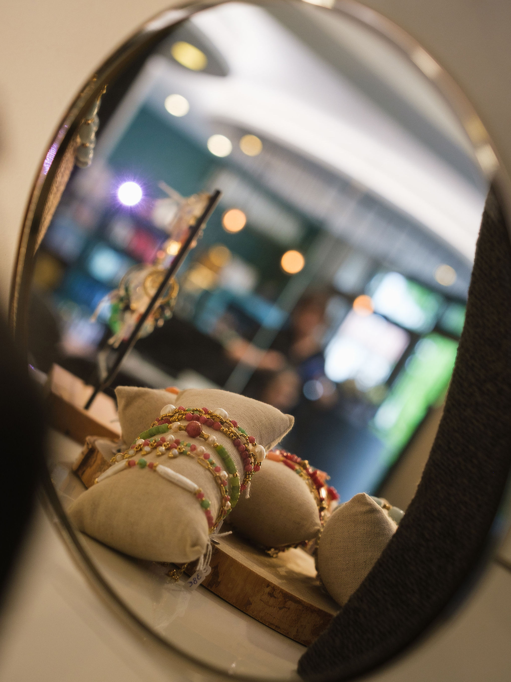 Colorful beaded bracelets displayed on fabric cushions reflected in a round mirror.