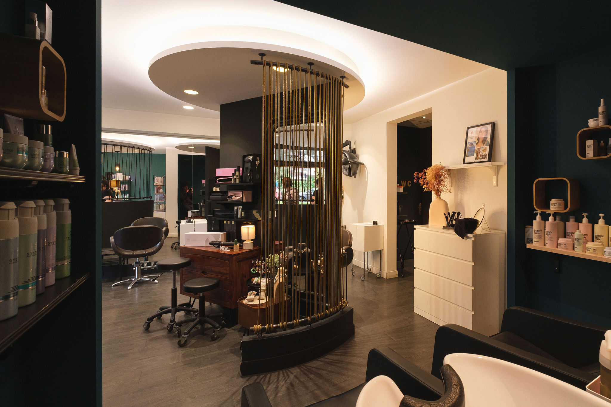 Modern hair salon interior with styling chairs, product shelves, and decorative lighting.